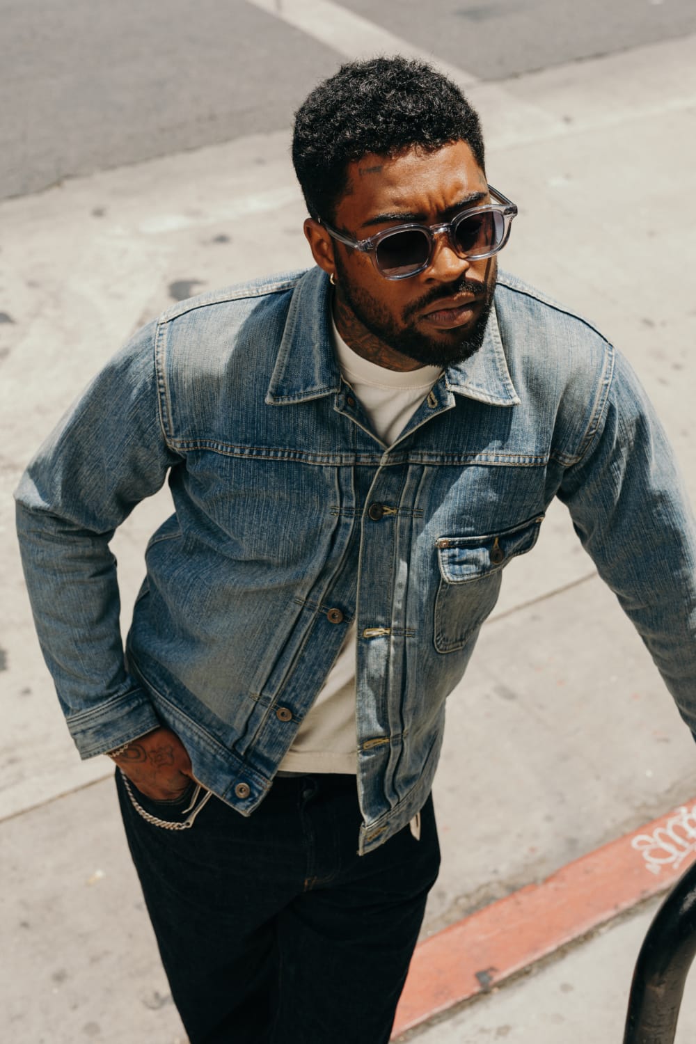 Man wearing a denim jacket and sunglasses on a city street.